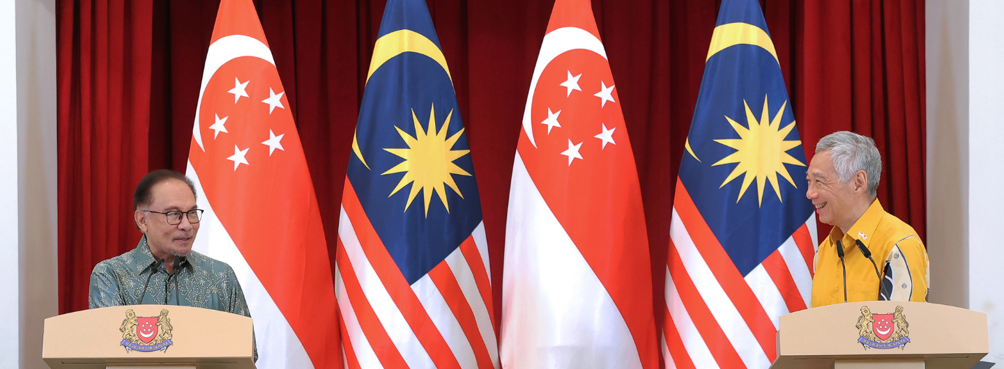 Anwar Ibrahim and Lee Hsien Loong at podiums with Malaysia and Singapore flags behind them.